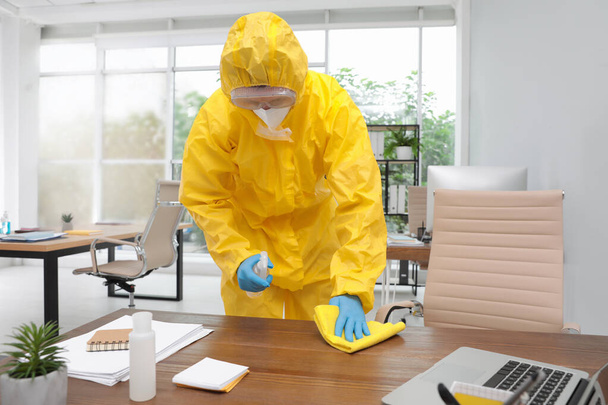 Janitor in protective suit disinfecting office furniture to prevent spreading of COVID-19 - Foto, immagini