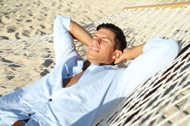 Handsome man relaxing in hammock on beach - 写真・画像