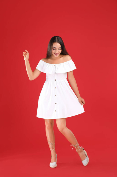 Young woman wearing stylish white dress on red background - Foto, imagen