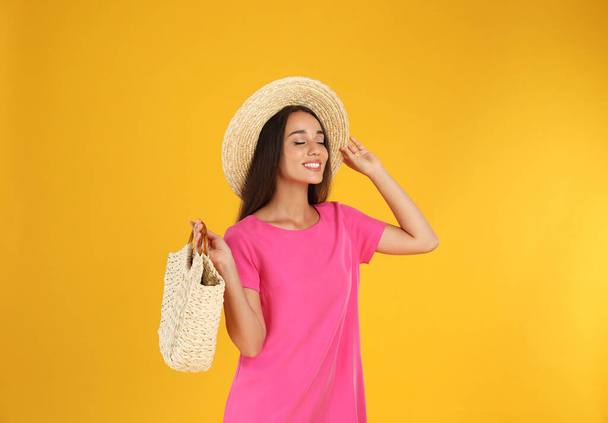 Young woman wearing stylish pink dress with straw bag on yellow background - Foto, Imagem