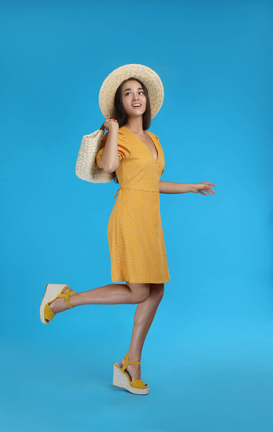 Young woman wearing dress with straw bag on light blue background - Foto, Imagem