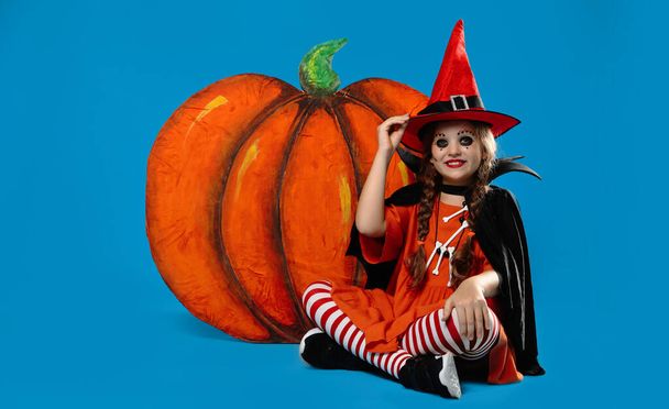Cute little girl with decorative pumpkin wearing Halloween costume on light blue background - Foto, imagen