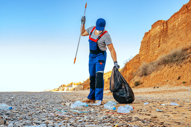 Man volunteer collecting garbage on the beach with a reach extender stick - Foto, afbeelding