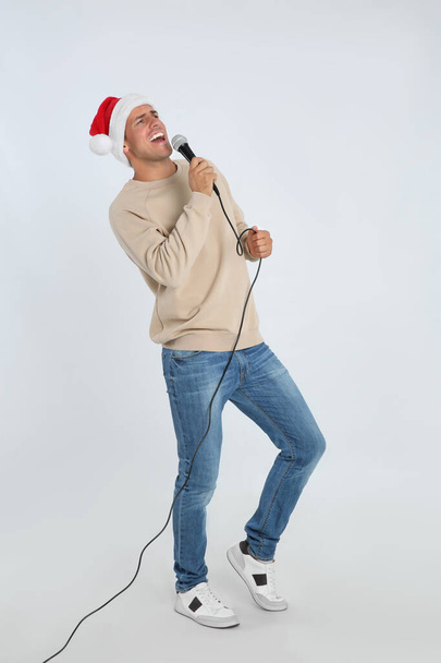Emotional man in Santa Claus hat singing with microphone on white background. Christmas music - Foto, Bild