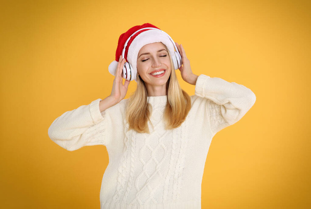 Happy woman with headphones on yellow background. Christmas music - Photo, Image