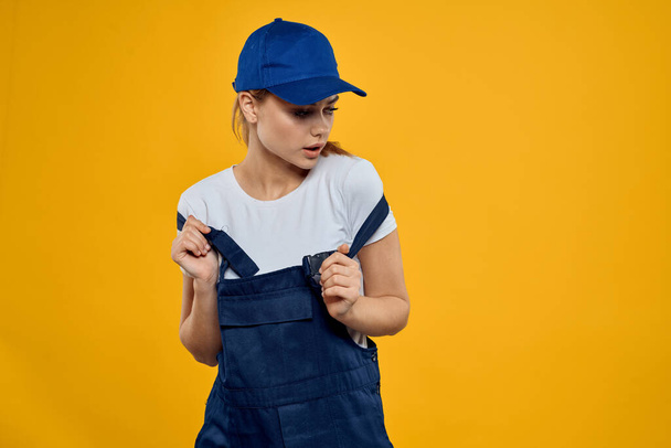 Woman in working uniform blue cap delivering courier service yellow background - Photo, Image