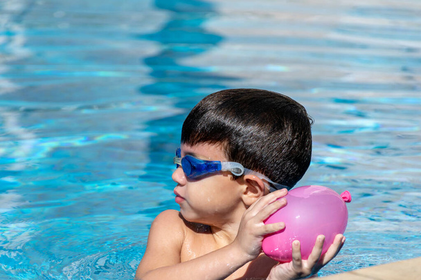 Detailní záběr chlapce s plaveckými brýlemi házející vodní balón. - Fotografie, Obrázek