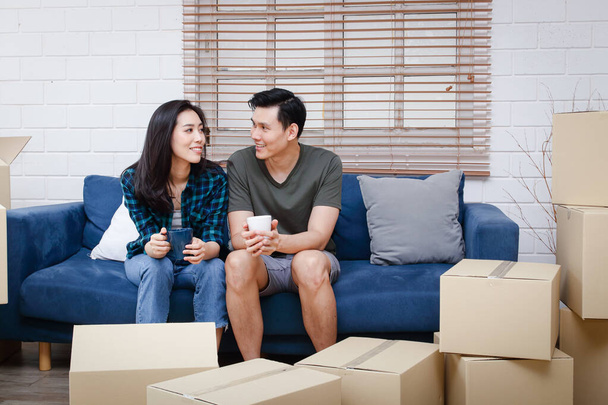 Aasialainen pari istuu sohvalla ja juuri muuttanut uuteen kotiin luoda lämmin perhe. Se on parin elämän alku. Kopioi tila - Valokuva, kuva