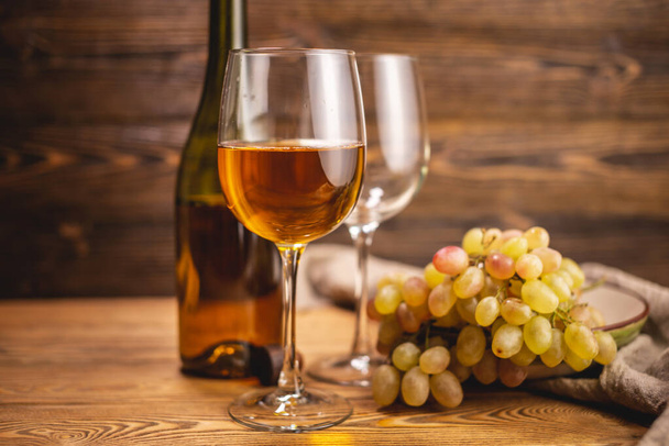 Пляшка сухого білого вина зі склянкою і гроном винограду на дерев'яному столі. Концепція виноградарства і виноробства
 - Фото, зображення