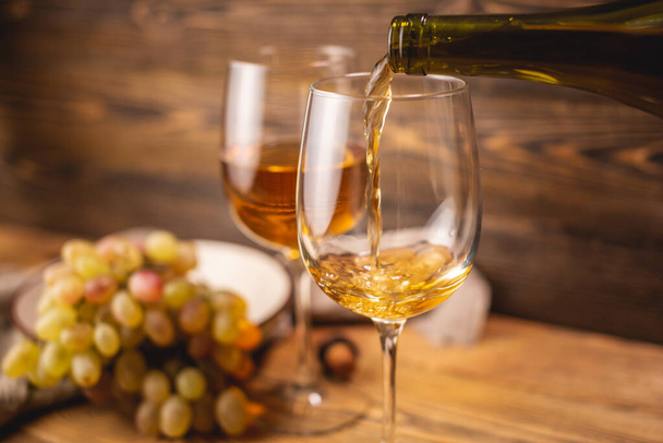 Láhev suchého bílého vína se sklenicí a hroznem na dřevěném stole. Koncept vinohradnictví a vinifikace - Fotografie, Obrázek