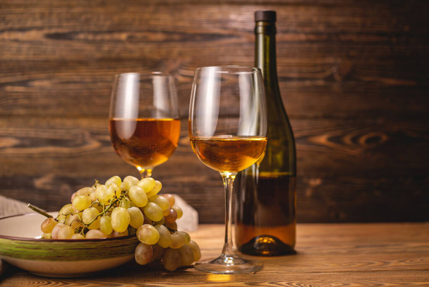 Una bottiglia di vino bianco secco con un bicchiere e un grappolo d'uva su un tavolo di legno. Concetto di viticoltura e vinificazione - Foto, immagini