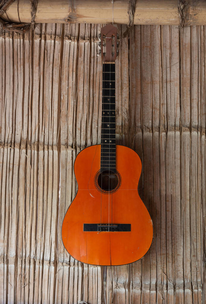 Orange acoustic guitar with strings hanging on a reed wall, closeup to the parts of the musical instrument - Фото, изображение