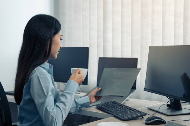 Mujer asiática estaba tomando café en la madrugada mientras contemplaba el programa y el código en la pantalla de la computadora. - Foto, imagen