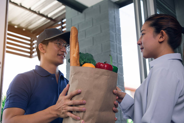 Dostawa azjatycki mężczyzna wręcza papierową torbę wewnątrz z warzywami lub żywności do azjatyckiej kobiety przed jego domem. - Zdjęcie, obraz