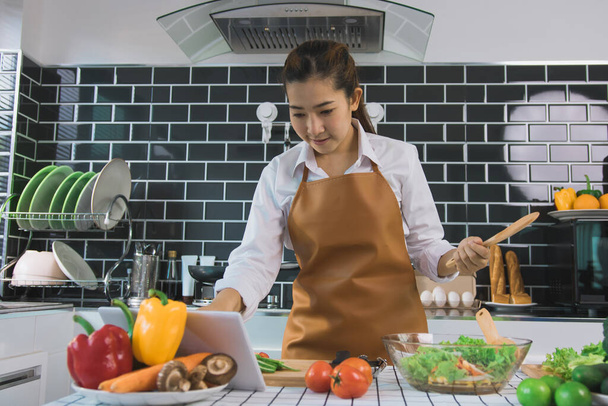 Las mujeres asiáticas están utilizando tabletas para encontrar recetas de sitios web de cocina en la mesa. - Foto, Imagen