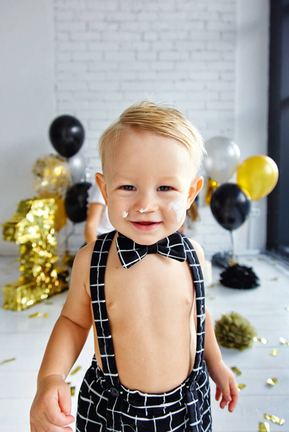 Mignon garçon blond à son premier anniversaire lors d'une fête décorée dans des couleurs or, noir et argent. Souillé dans le gâteau - Photo, image