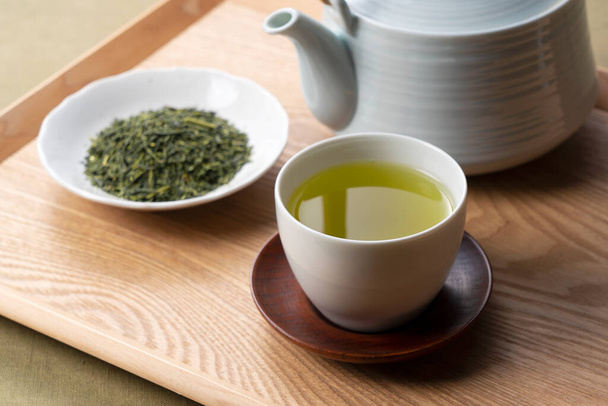 Green tea and tea leaves placed on a wooden tray. Japanese green tea image - Φωτογραφία, εικόνα
