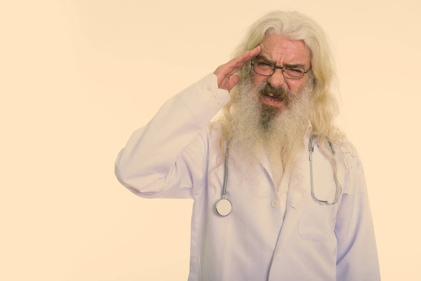 Studio shot of handsome senior man doctor with long white curly beard and hair isolated against white background - Фото, изображение