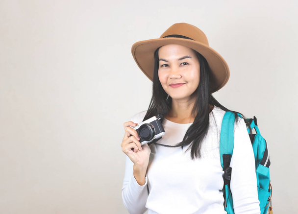 Portret Azjatki w białej koszulce i kapeluszu, trzymającej kamerę i niosącej plecak, uśmiechniętej i patrzącej w kamerę. Koncepcja podróży. - Zdjęcie, obraz