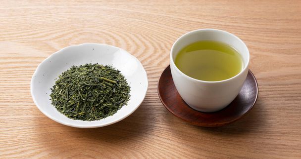 Zielona herbata i liście herbaty umieszczone na drewnianej tacy. Japoński obraz zielonej herbaty - Zdjęcie, obraz