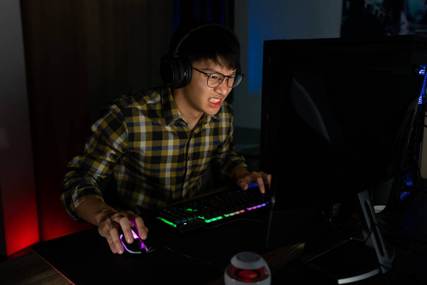 関与アジアの男性サイバースポーツゲーマーは、自宅で夜の暗い部屋でコンピュータ上でビデオゲームをプレイ集中しました, eスポーツと技術の概念. - 写真・画像