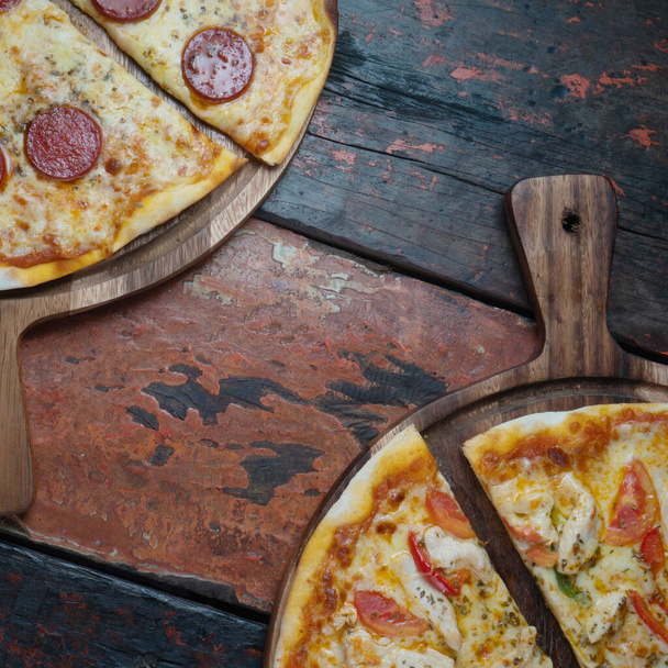 Vista superior de las sabrosas pizzas frescas sobre fondo de madera. Una pizza con salchicha turca y queso mozzarella, otra con pollo, pimentón y tomate aislados sobre mesa rústica de madera
 - Foto, Imagen