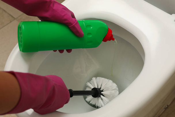 Woman in rubber pink gloves cleans toilet bowl with brush - Foto, immagini