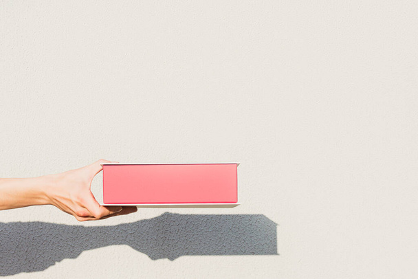 La mano de una persona sostiene una caja de regalo roja hecha de papel grueso sobre un fondo claro - Foto, Imagen