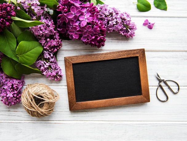 Fresh lilac flowers frame over wooden background with copy space on blackboard, flat lay floral composition - Valokuva, kuva