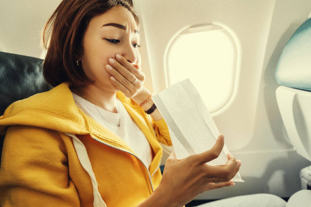Una viajera asiática sufre un ataque agudo de náuseas durante la turbulencia en un avión. La mujer estaba mareada y airsock durante el vuelo aéreo - Foto, imagen