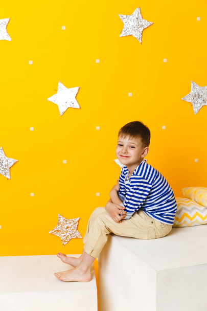 Little boy sitting on a white cube on yellow background with stars - Foto, afbeelding