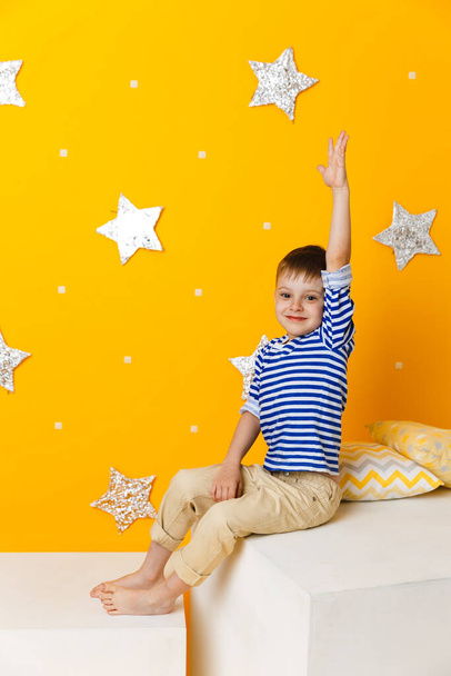 Little boy sitting on a white cube on yellow background with stars - Foto, Imagen