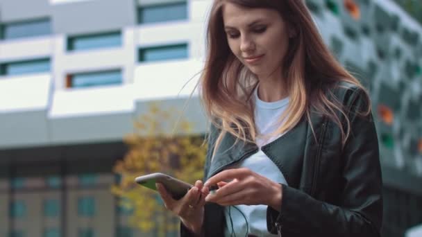 Attraktives Mädchen, Studentin, in moderner Kleidung Verwendet ein Handy, um Gute-Laune-Musik zu hören, legt Musikliebhaber ein Lieblingslied, glückliche Frau verwendet Roaming, High-Speed-Verbindung 5G - Filmmaterial, Video