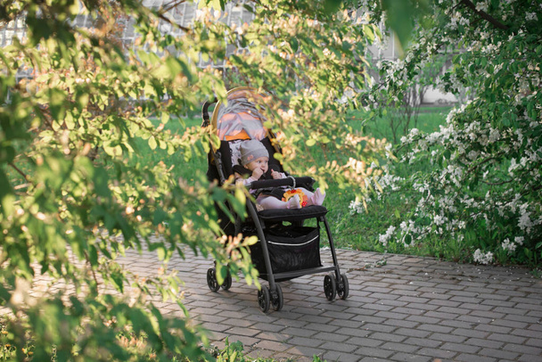 A girl in pink clothes is sitting in a yellow stroller in a Park among green trees. - Фото, зображення