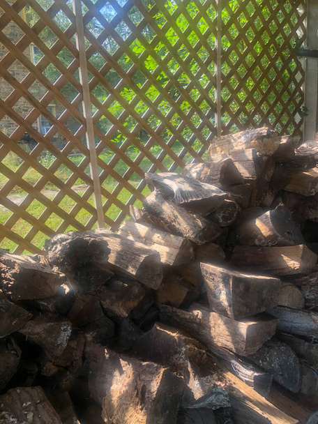 Gesnipperd brandhout gestapeld achter tuinrooster en gekapt zonlicht. - Foto, afbeelding