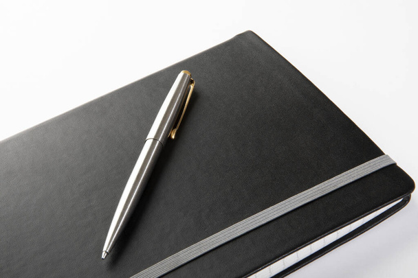 Custom silver ballpoint pen on modern black journal on a white background. - Fotografie, Obrázek
