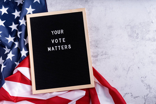 Black letter board with the text your vote matters with American flag on white marble background - Фото, зображення