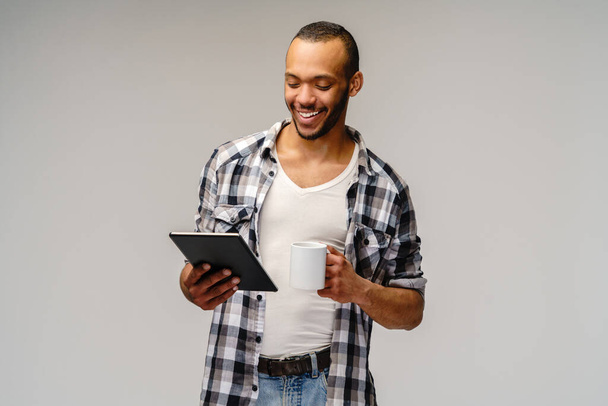 Portrait of a young african american man wearing casual shirt holding tablet pc pad and cup of coffee - Fotoğraf, Görsel