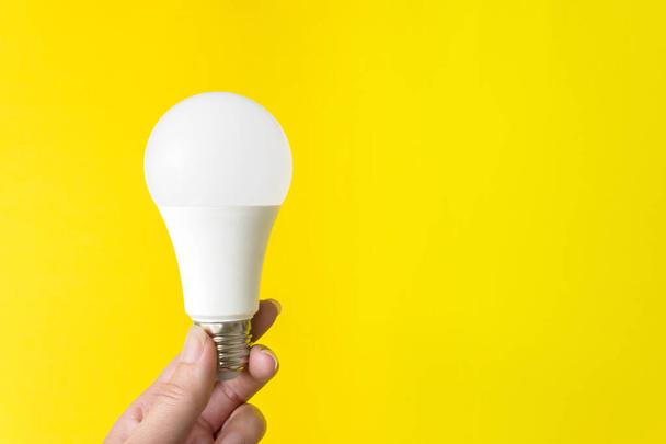 Una lampadina in mano su fondo giallo. Nuova tecnologia dell'energia. Copia spazio - Foto, immagini