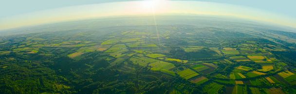 Вид зверху, широка панорама, підсвічування сонця над зеленим горбистим пейзажем, кілька оброблюваних ділянок серед лісових дерев на ранньому світанку, туман, туман
. - Фото, зображення