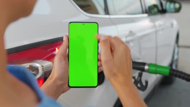 Woman uses a mobile application in a smartphone to pay for refueling a car. Smartphone with a green screen. Chroma key - Footage, Video