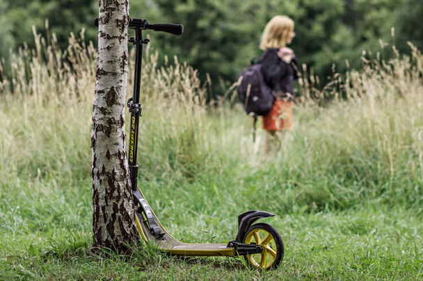 A young woman with a scooter walks in a summer Park. - Foto, imagen