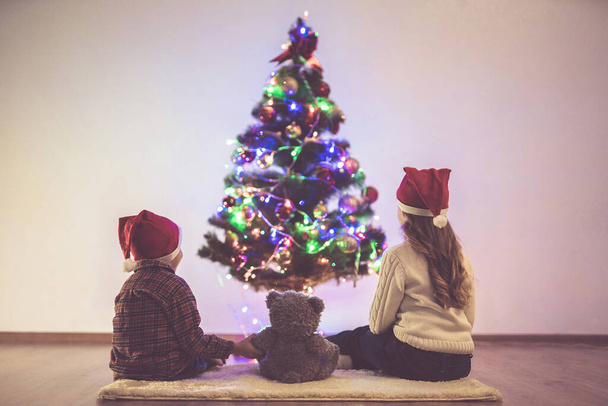 Oyuncak ayılı çocuklar Noel ağacının yanında oturuyorlar. - Fotoğraf, Görsel