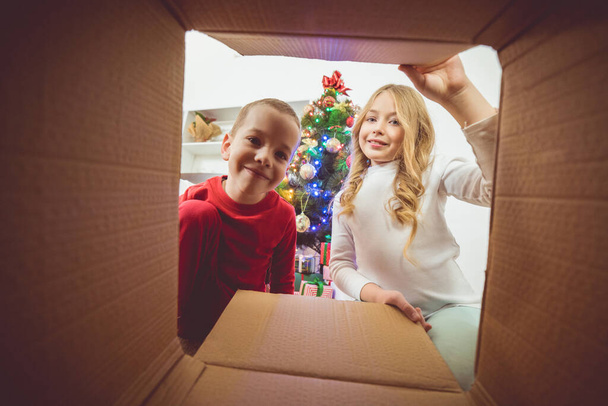 El niño y una niña abren la caja en el fondo del árbol de Navidad - Foto, imagen