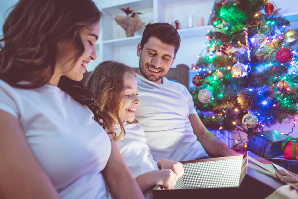 Die glückliche Familie öffnet die Geschenkbox neben dem Weihnachtsbaum. Abend Nacht - Foto, Bild