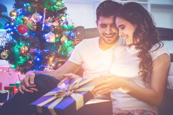 Το ζευγάρι ξεπακετάρει το κουτί δώρου στο φόντο του χριστουγεννιάτικου δέντρου - Φωτογραφία, εικόνα