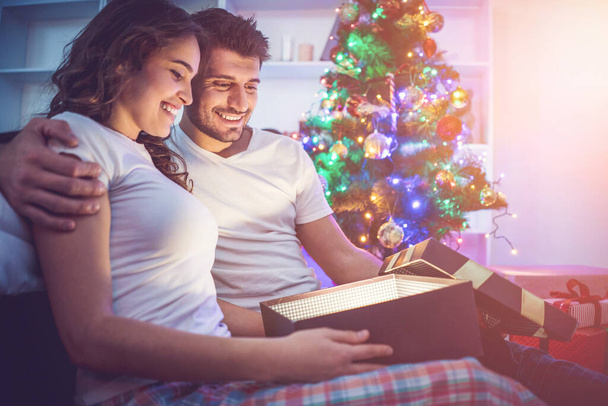 Der glückliche Mann und eine Frau öffnen den Leuchtkasten neben dem Weihnachtsbaum - Foto, Bild