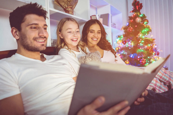 A família feliz leu o livro na cama perto da árvore de Natal. hora da noite - Foto, Imagem
