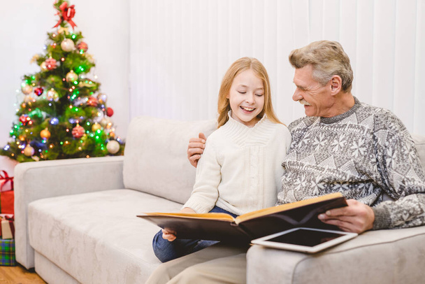 La chica con un abuelo leyó el libro cerca del árbol de Navidad. - Foto, imagen