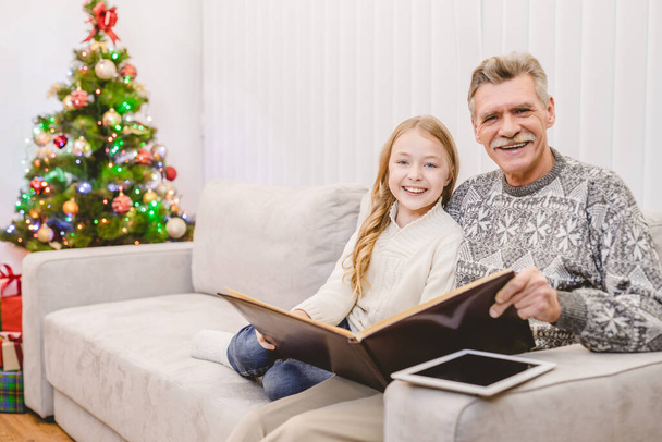Das lächelnde Mädchen mit dem Großvater las das Buch am Weihnachtsbaum - Foto, Bild
